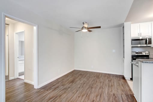 an empty living room with a ceiling fan and a kitchen