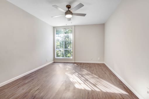 an empty living room with a ceiling fan and a window