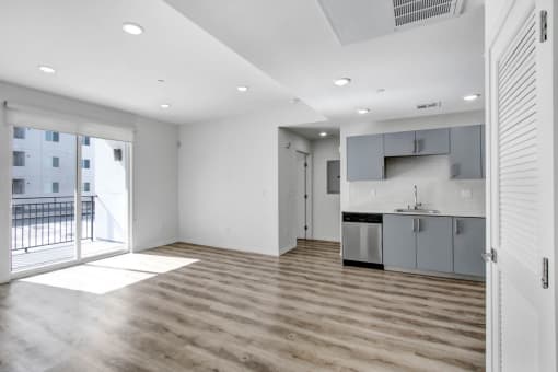 an empty living room with a kitchen and a balcony