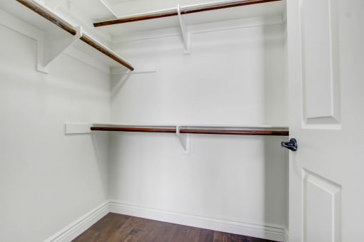 a walk in closet with white walls and a white closet door with a wood floor