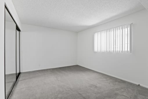 the spacious living room of an apartment with white walls and a window