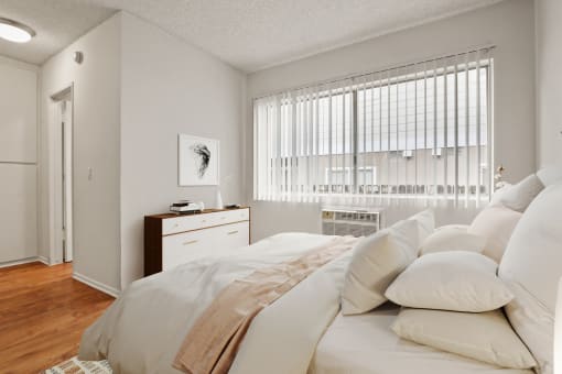 a bedroom with white bedding and pillows and a window