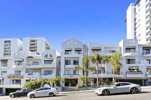 an apartment building with palm trees and cars parked in front of it