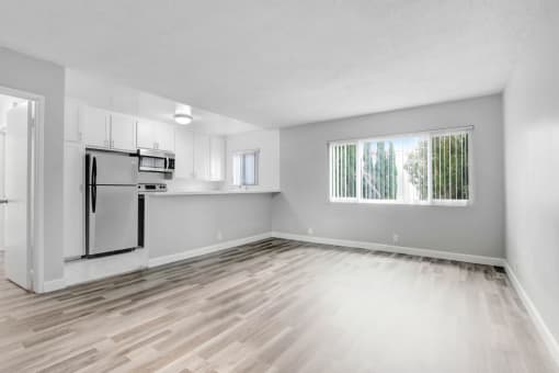 the living room and kitchen of an empty apartment with wood flooring and a window