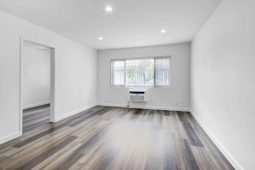 a living room with white walls and wooden floors and a window