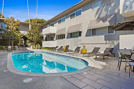 a swimming pool in front of a building with chairs and a resort style pool