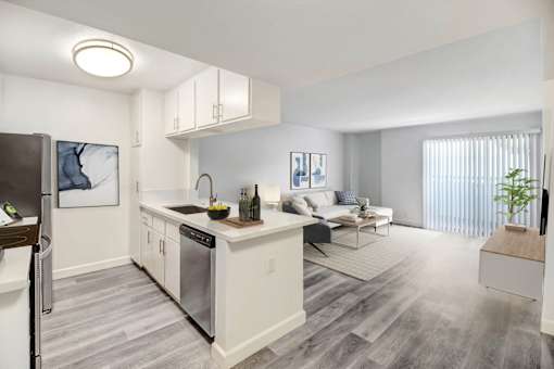 A modern kitchen with a refrigerator on the left and a dining area with a white couch and a coffee table.