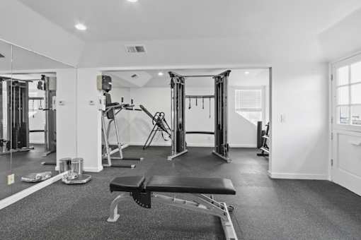 A black and white photo of a gym with a bench, weights, and exercise equipment.