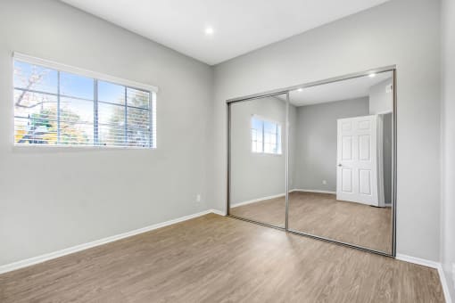 an empty bedroom with a mirrored closet door and a window