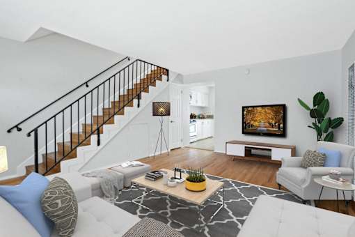 a living room with white furniture and a staircase in the background