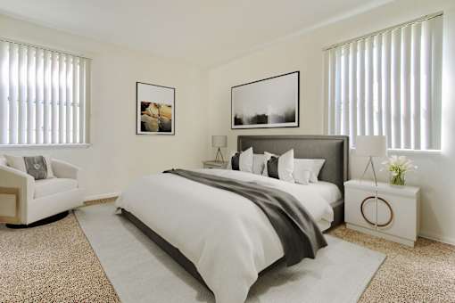 A bedroom with a large bed, a white armchair, and two framed pictures on the wall.