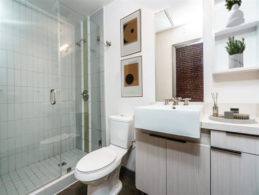 Apartments For Rent In Downtown Los Angeles, CA - Broadway Lofts - Bathroom With A Large Vanity Mirror, Sink, Wood-Grain Like Cabinets, A Toilet, Tile Backsplash, And A Shower With Tub