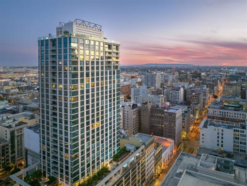 a cityscape with a tall skyscraper in the foreground and a sunset in the background