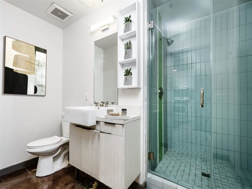 DTLA Apartments - Broadway Lofts - Bathroom With Modern Sink, Shelves, And Walk In Glass Shower With Tile