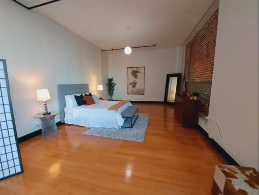 Dog-Friendly Apartments In Downtown Los Angeles, CA - Mercantile Lofts - Spacious Living Area With Bamboo Wood Flooring, High Ceilings, Contemporary Lighting Fixtures, And Exposed Brick Wall.
