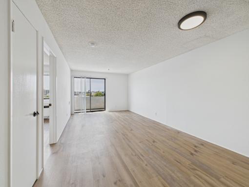 A room with a white ceiling and wooden flooring with a door on the left.