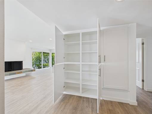 A white shelving unit is open in a room with wood flooring.