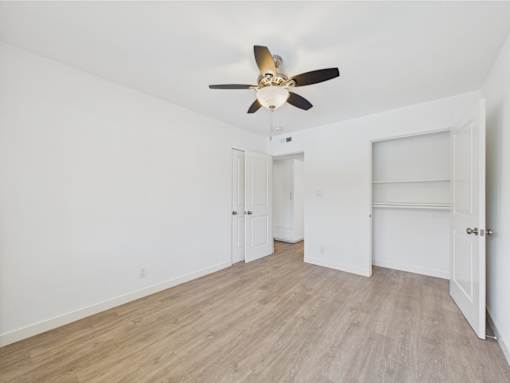 A room with a ceiling fan and light fixture, two doors, and a windowless wall.