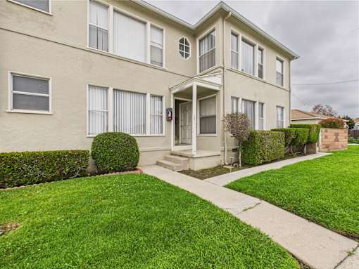 A beige two-story house with a front porch and a green lawn.