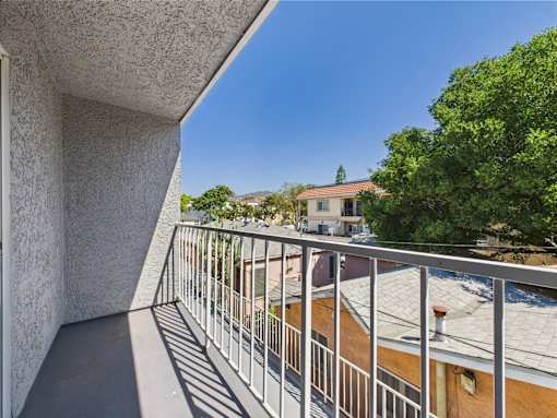 A balcony with a metal railing and a view of a building and trees.