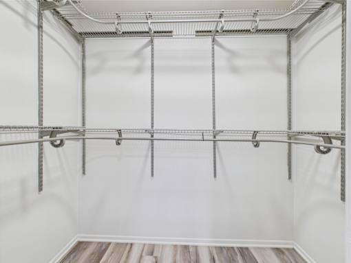 A white walk-in closet with a wooden floor and metal shelving.