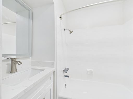 A white bathroom with a sink, mirror, and bathtub.