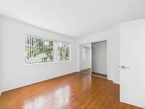 A room with a white door and a window with a view of trees.