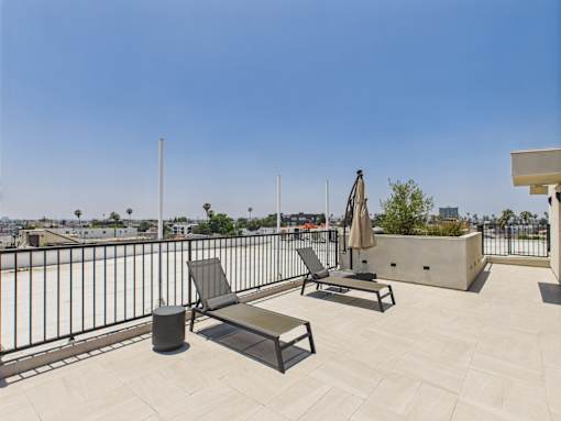 A patio with a black metal railing, two chairs, a table, and a trash can.