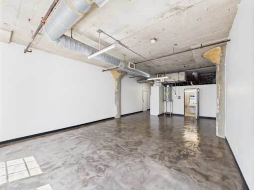 A large empty room with a concrete floor and exposed pipes on the ceiling.
