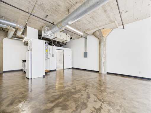 A room with a concrete floor and ceiling with white walls and a few white cabinets.