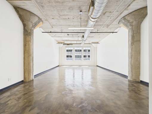 A large empty room with concrete floors and arched columns.