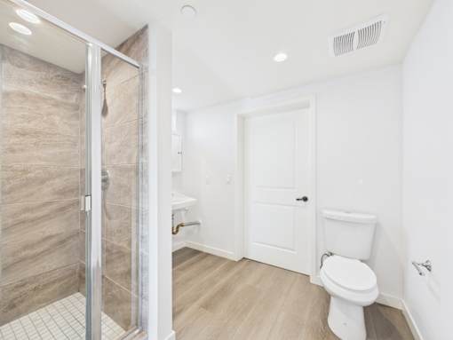 A white toilet sits in a bathroom with a walk-in shower.