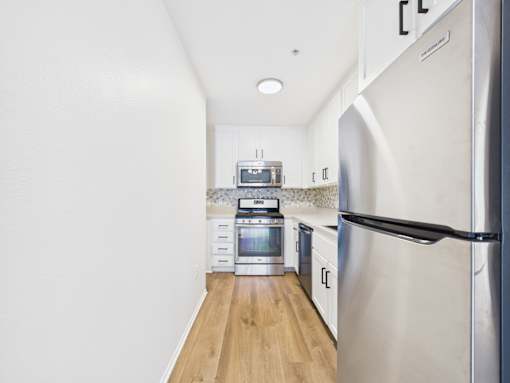 A kitchen with a refrigerator on the right and a microwave and oven on the left.