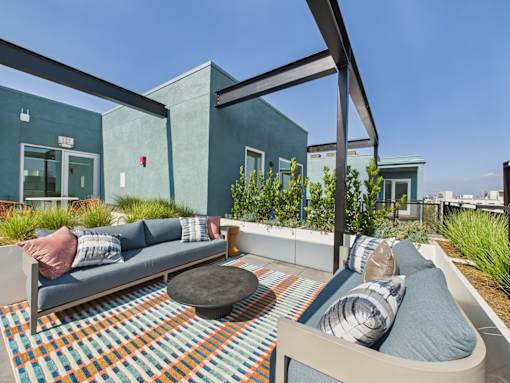 A modern outdoor seating area with a blue couch and a round ottoman.