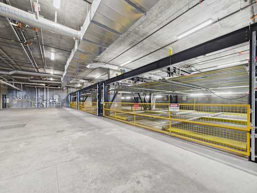 A large, empty industrial space with a concrete floor and yellow safety barriers.