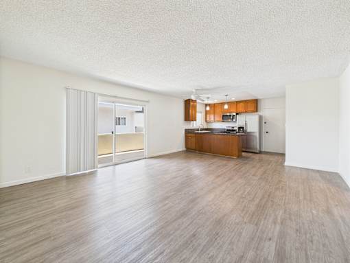 A spacious room with wooden flooring and a kitchen area in the background.
