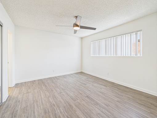 A room with a ceiling fan and light, hardwood floors, and a window with blinds.