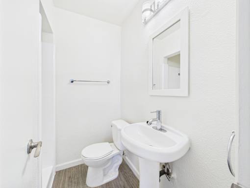 A white bathroom with a toilet, sink and mirror.
