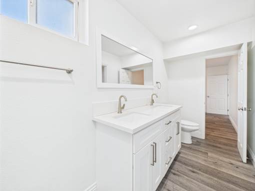 A white bathroom with a wooden floor and a large mirror.