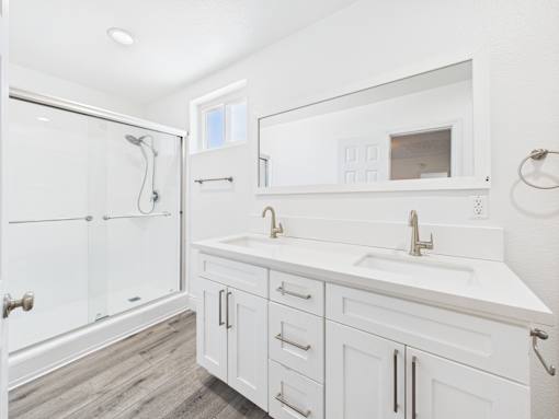 A white bathroom with a walk-in shower and double sink vanity.