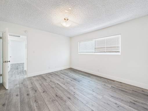 A room with a wooden floor and a window with blinds.