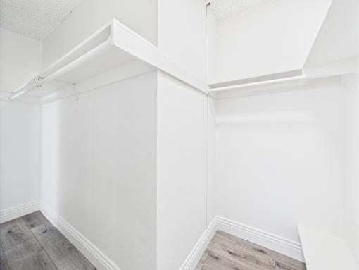 A white wall with a corner shelf and a grey floor.