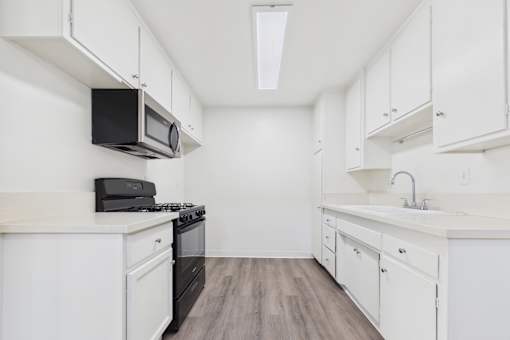 A kitchen with white cabinets and a black microwave.