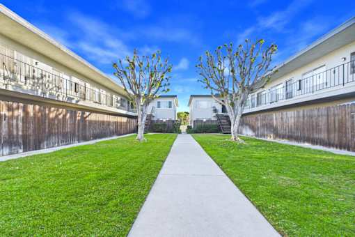 A long concrete walkway leads between two buildings with green grass on either side.