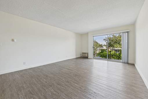 A room with wooden flooring and a sliding glass door leading to a balcony.