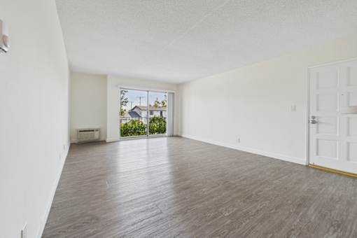 A room with wooden flooring and a sliding glass door leading to a balcony.