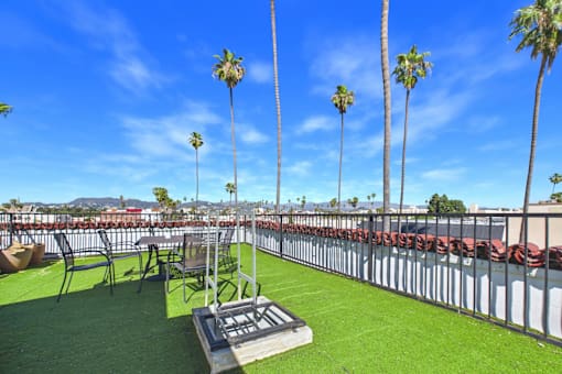 A rooftop patio with a table and chairs and palm trees.
