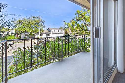 A balcony with a metal railing and a view of a street and houses.