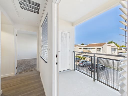 A balcony with a metal railing and a view of a parking lot and houses.