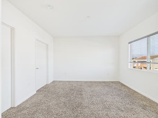 A room with a carpeted floor and a window with blinds.